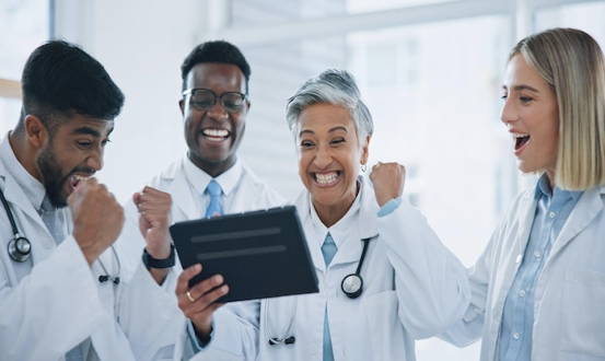 Group of smiling medical professionals collaborating on a tablet, representing Qualified Medical Evaluators in California discussing strategies to market themselves effectively in the workers' compensation field.