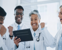 Group of smiling medical professionals collaborating on a tablet, representing Qualified Medical Evaluators in California discussing strategies to market themselves effectively in the workers' compensation field.